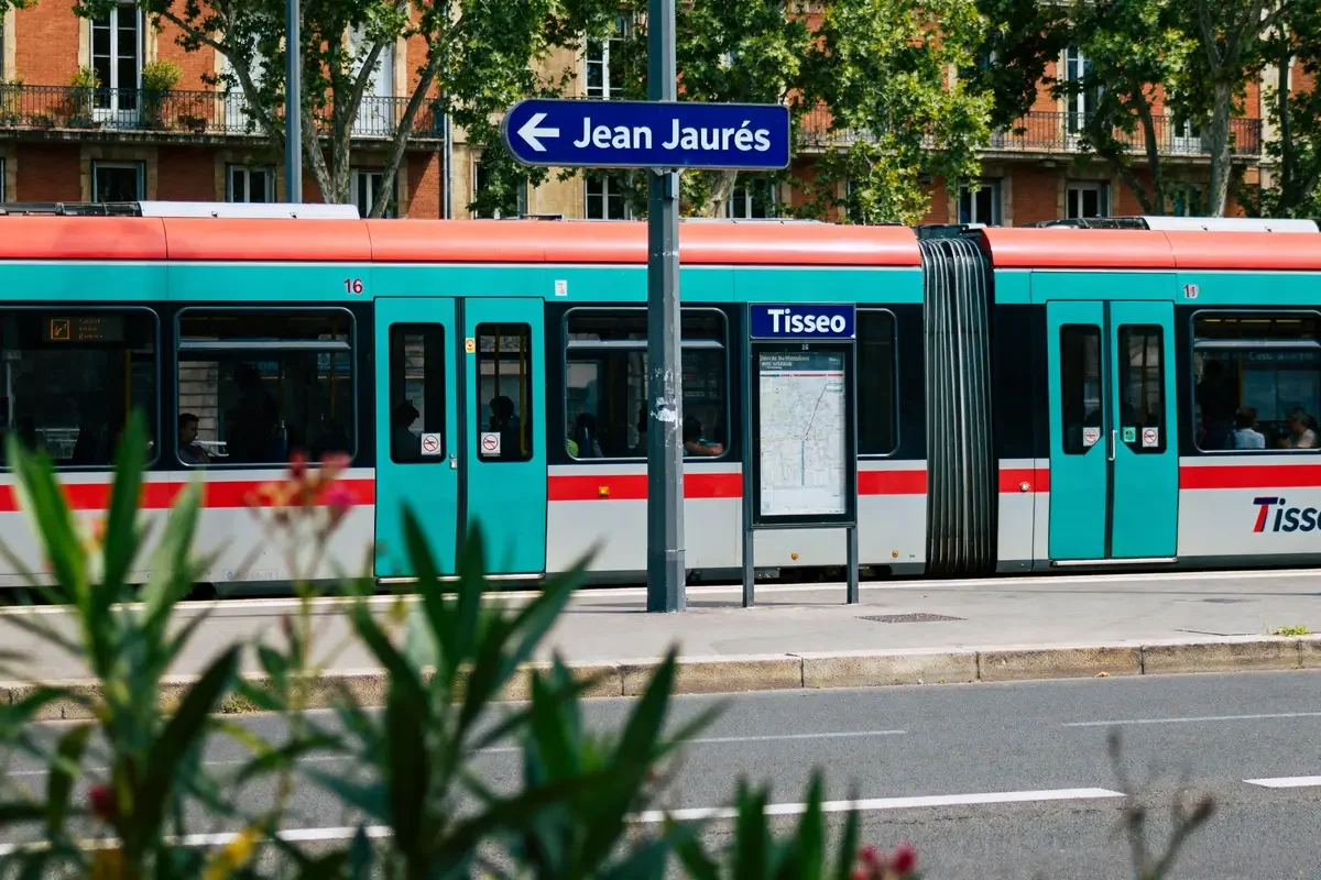 Tramway Tisséo passant près d'un panneau de signalisation Jean Jaurès, arbres et feuillage au premier plan.