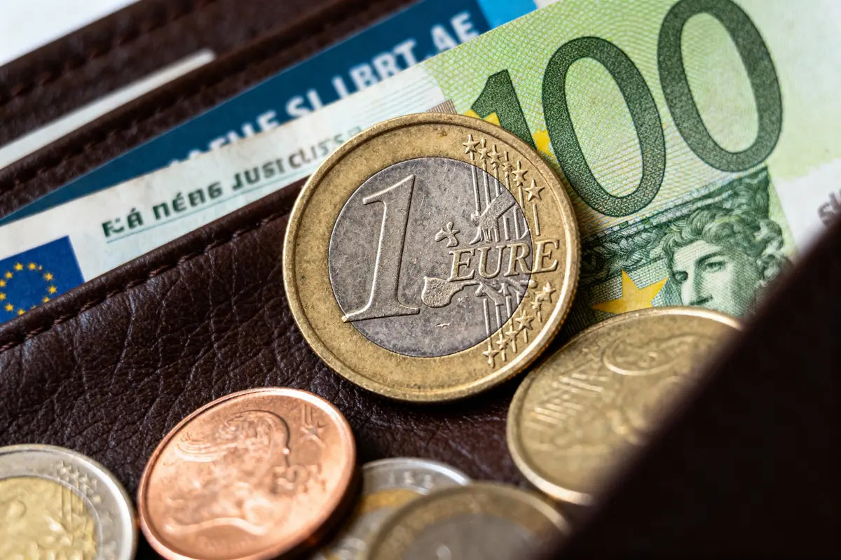 Pièces de monnaie euro et billet cent euros partiellement visibles dans un portefeuille marron.