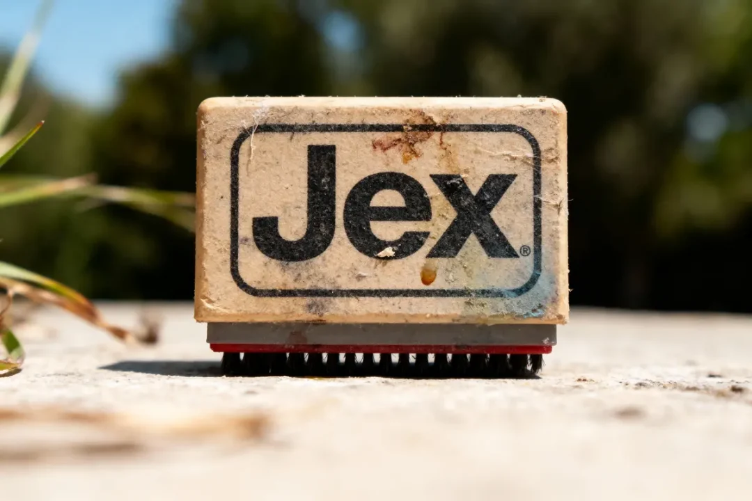 Brosse de nettoyage Jex usée sur surface en béton, arrière-plan flou et herbe à gauche.