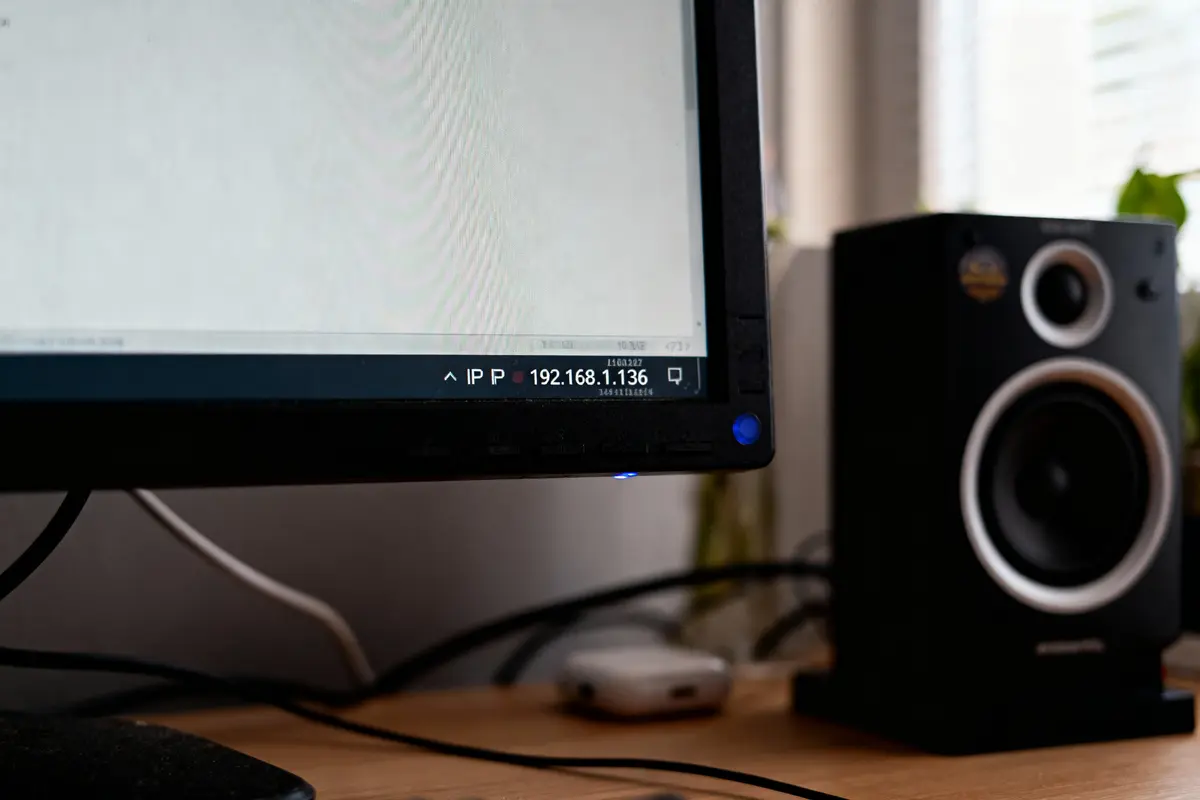 Écran avec adresse IP affichée, enceintes noires, câbles connectés sur un bureau en bois.