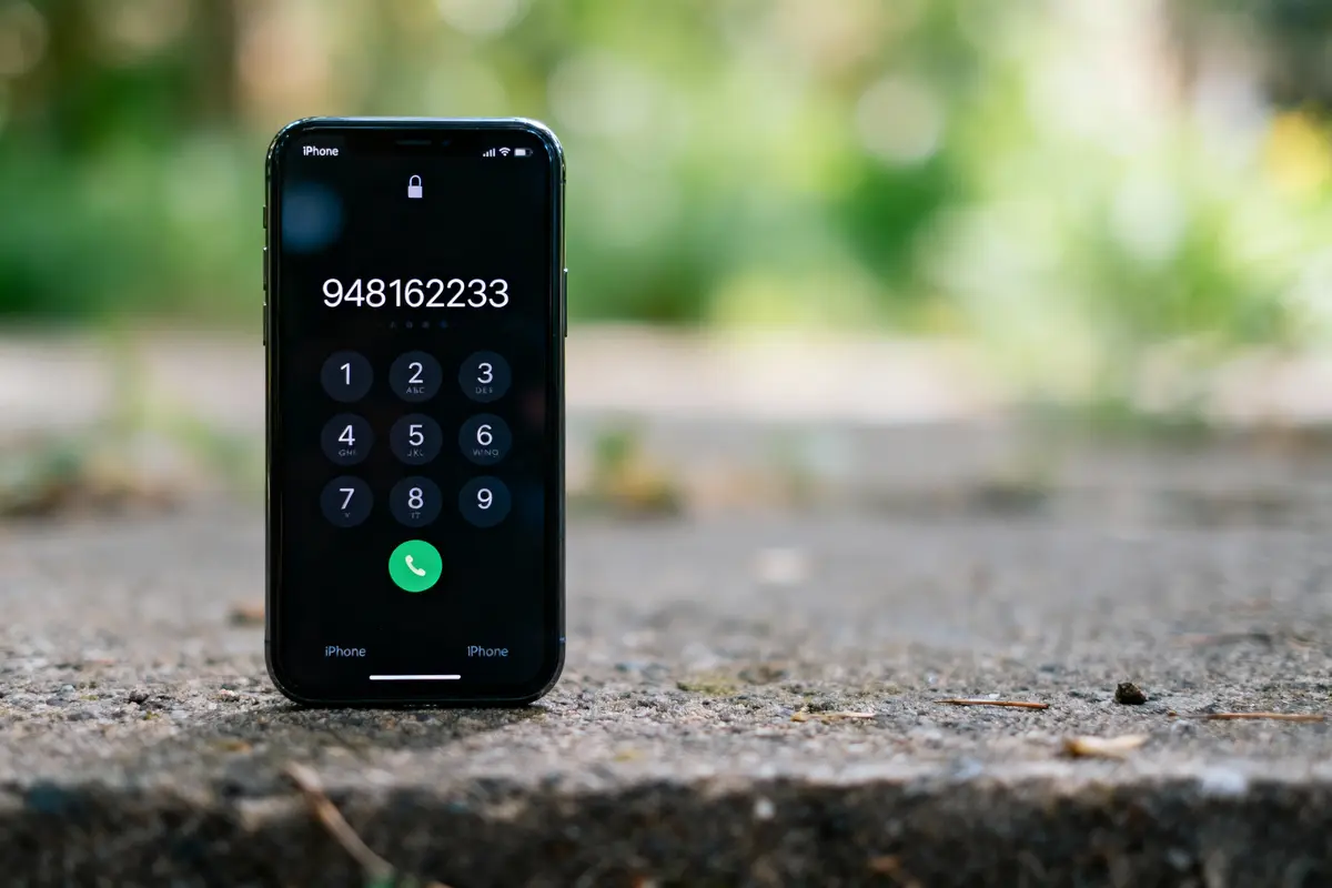 iPhone affichant un numéro de téléphone sur l'écran, posé sur une surface extérieure floue.