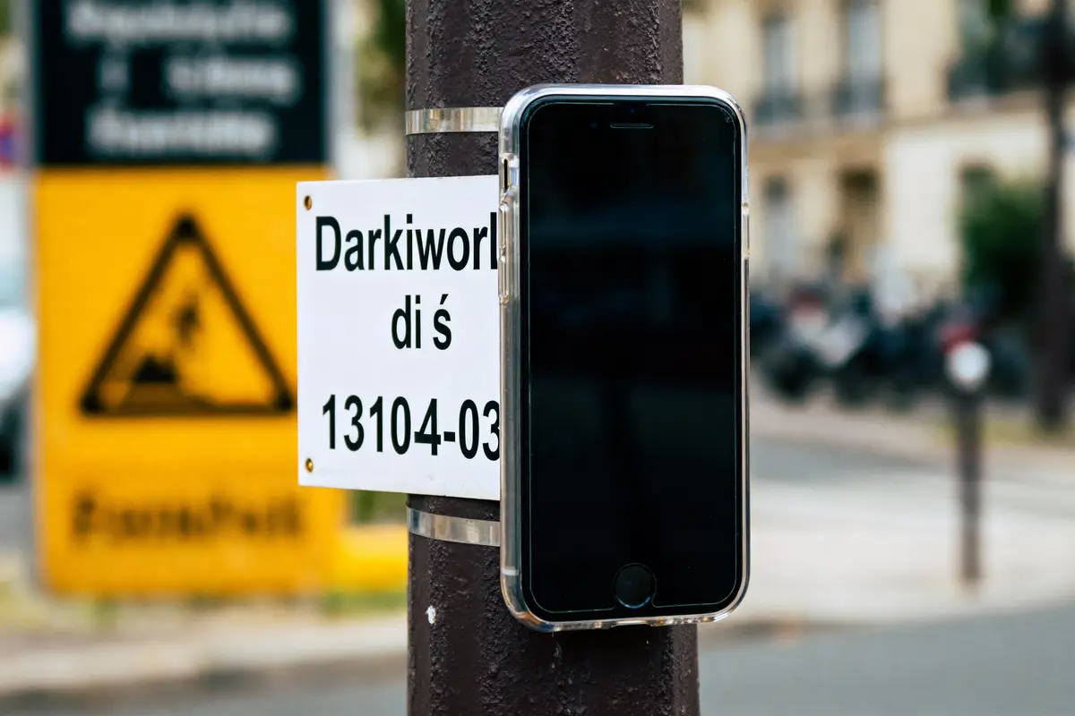 Téléphone attaché à un poteau devant un panneau de rue, avertissement routier en arrière-plan flou.