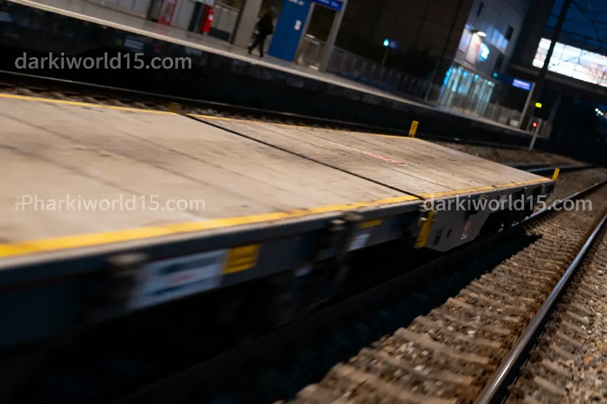 Plateforme de train à quai vide la nuit, avec un wagon en mouvement rapide au premier plan.