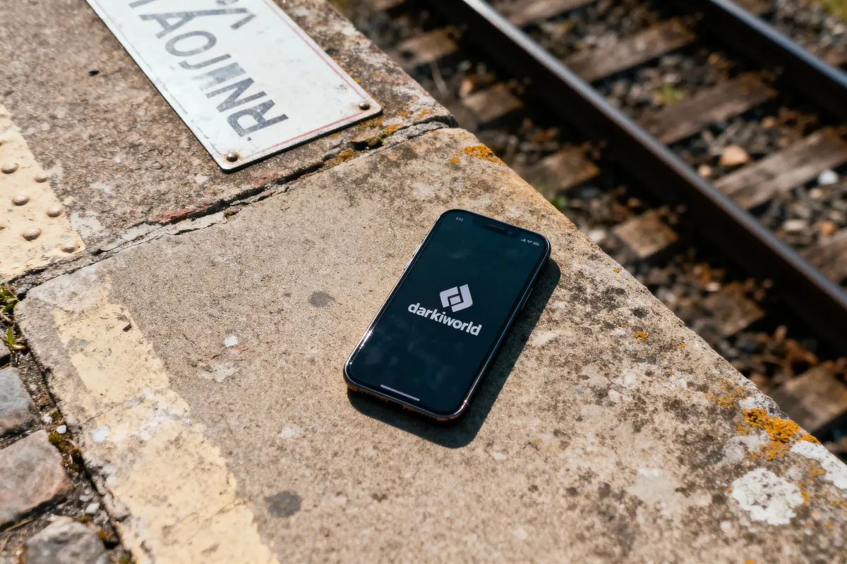 Smartphone avec écran allumé, posé sur un quai de gare en béton près des rails.