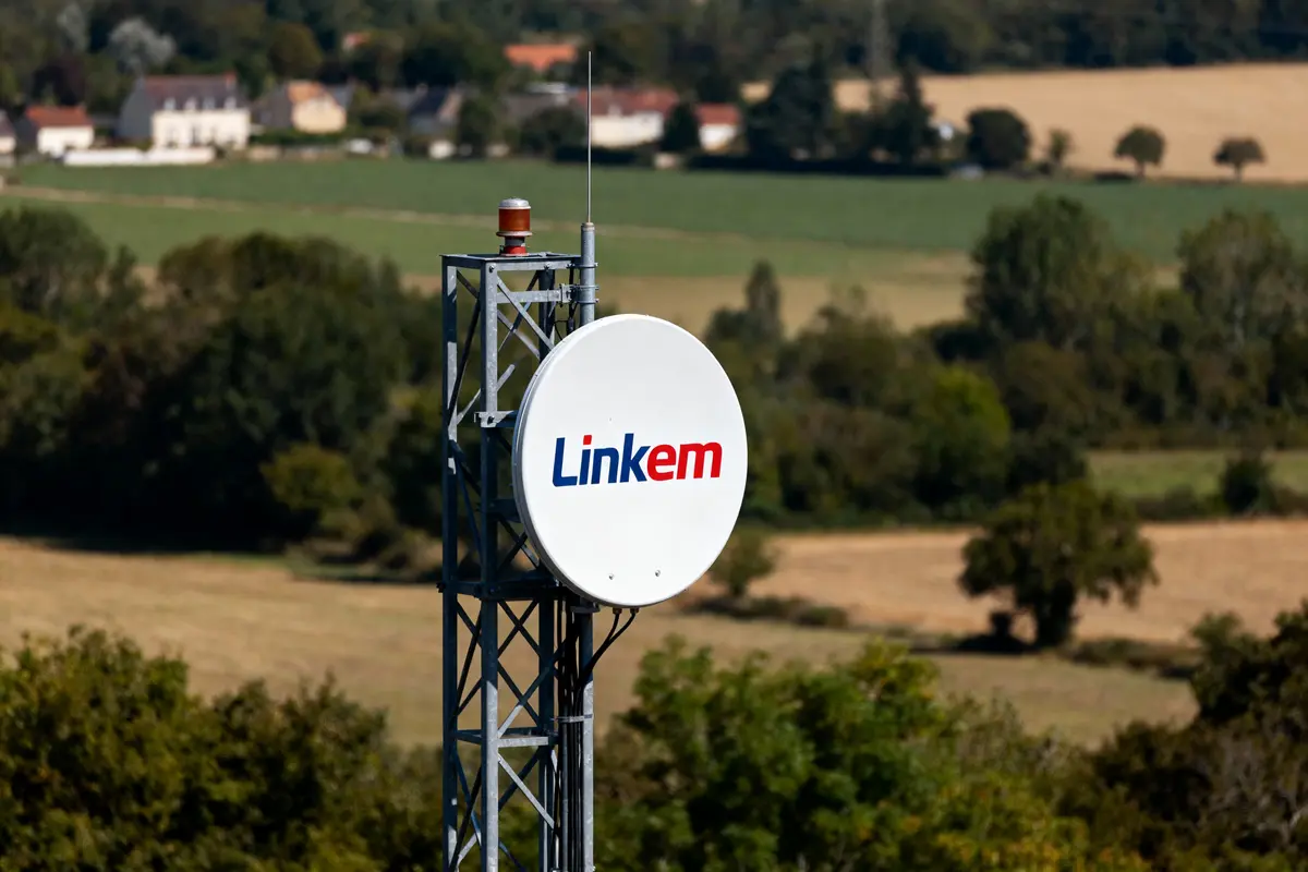 Antenne Linkem blanche sur pylône métallique, paysage rural en arrière-plan avec champs et arbres.