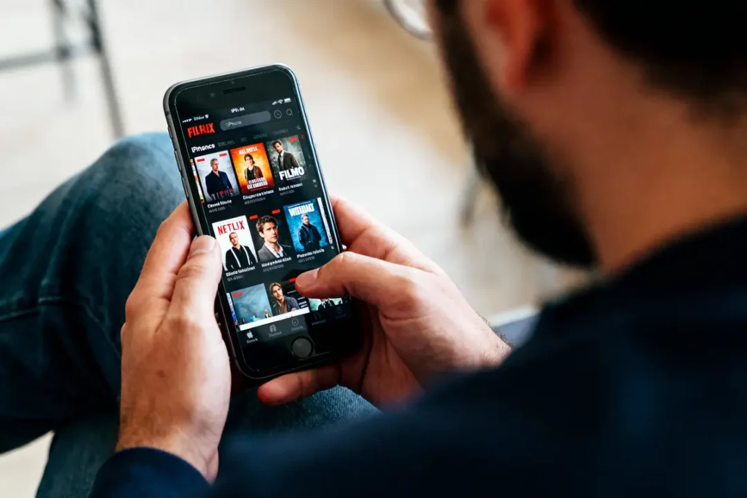 Personne utilisant un smartphone pour naviguer sur une application de streaming vidéo, affichant plusieurs films et séries.