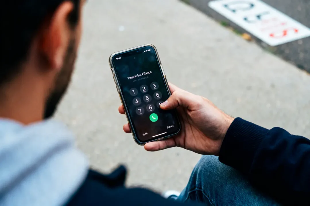 Personne tenant un smartphone avec écran de numérotation d'appel, texte "téléphone" visible, prise extérieure.