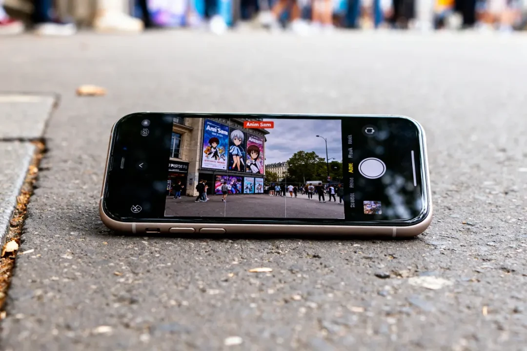 Smartphone affichant des affiches Anim Sama sur un bâtiment en arrière-plan urbain