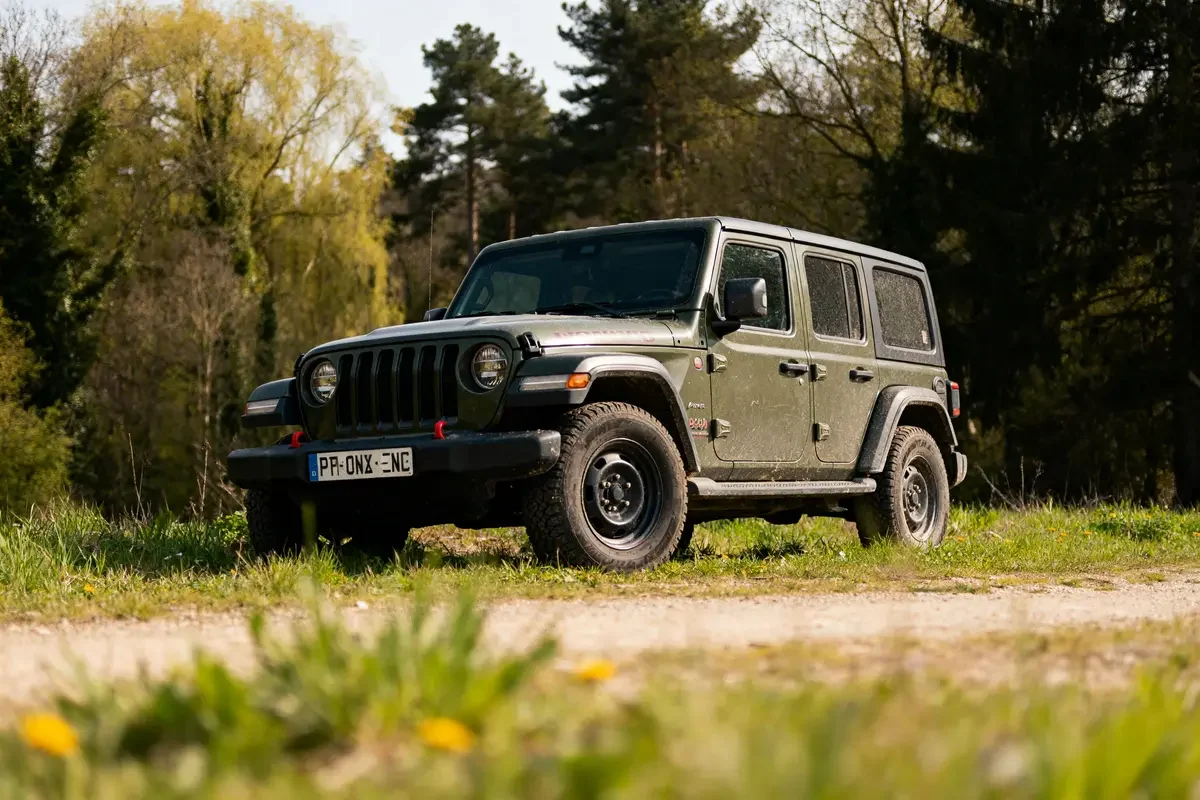 Jeep verte tout-terrain arrêtée dans un chemin forestier en arrière-plan tirexo