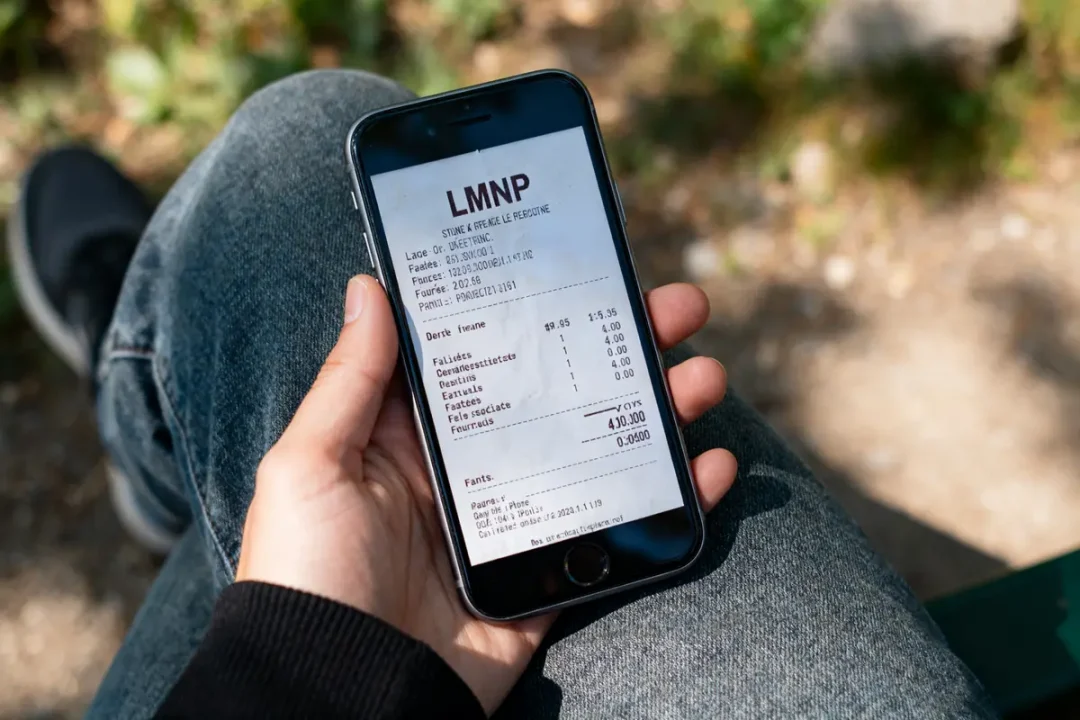 Personne tenant un smartphone affichant un ticket de caisse LMNP numérisé sur l'écran