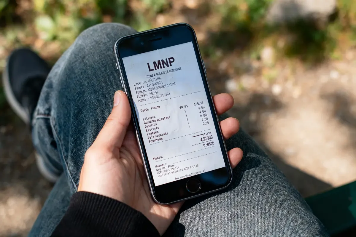 Personne tenant un smartphone affichant un ticket de caisse LMNP numérisé sur l'écran