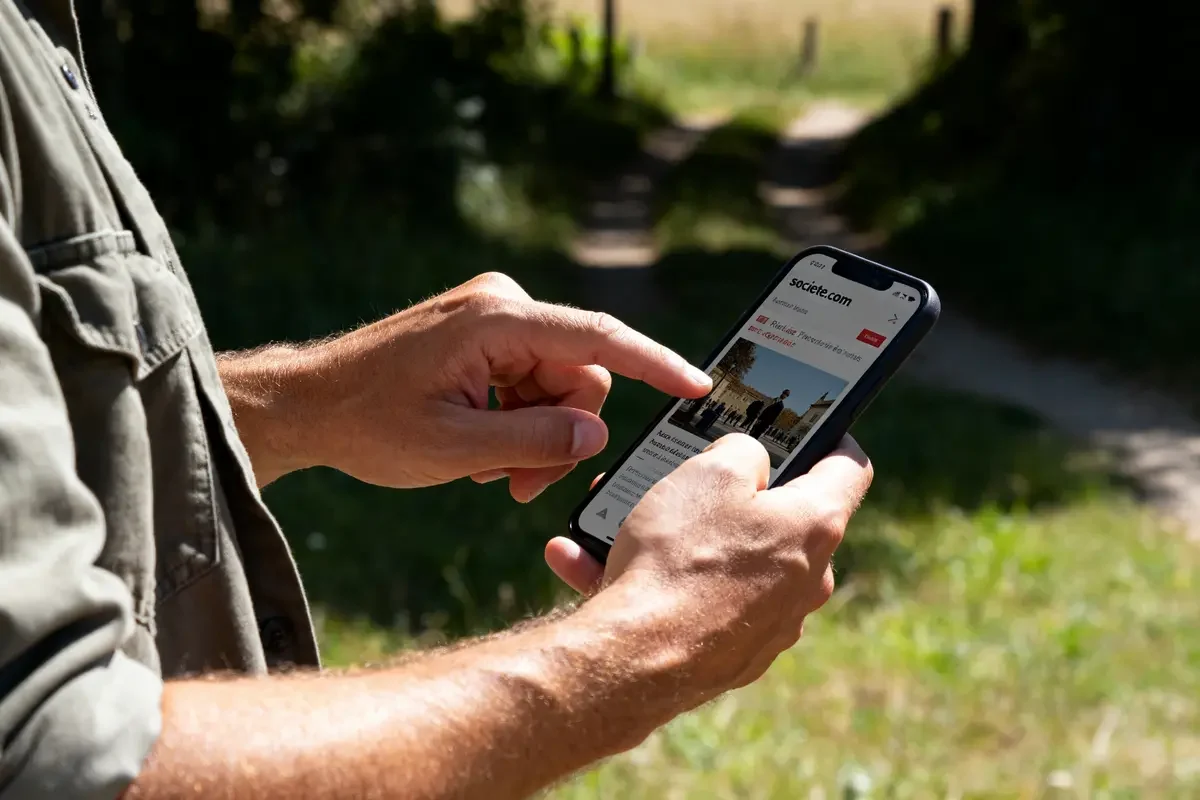 Personne consultant societe.com gratuit sur un smartphone en extérieur par une journée ensoleillée