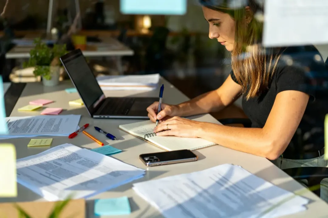 Secrétaire indépendante rédigeant au bureau avec ordinateur et documents reflétant son slogan professionnel efficace