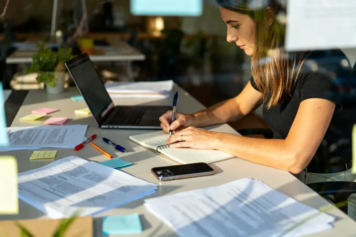 Secrétaire indépendante rédigeant au bureau avec ordinateur et documents reflétant son slogan professionnel efficace